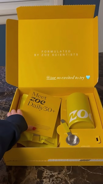 An intimate, top-down perspective capturing the moment a branded daily supplement box is opened, revealing the product components.